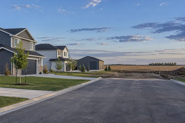 New suburban street ending at graded bare ground with cropland starting immediately beyond