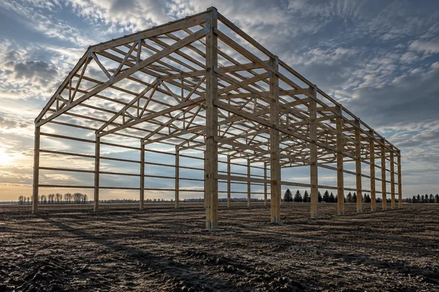 Complete post-frame skeleton of columns, trusses and purlins against a prairie sky before cladding